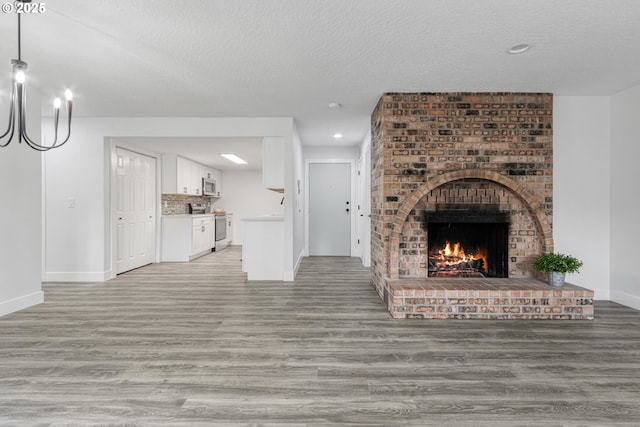 unfurnished living room featuring a brick fireplace, light wood-style flooring, baseboards, and a textured ceiling