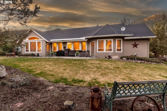 rear view of house with a shingled roof, a patio, and a lawn