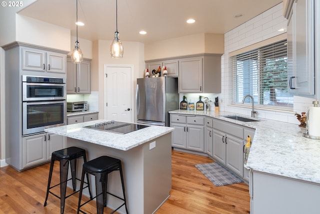 kitchen featuring a center island, gray cabinetry, appliances with stainless steel finishes, a sink, and light wood-type flooring