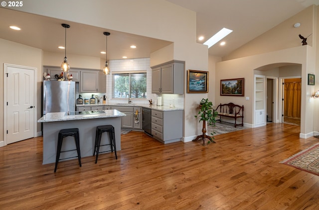 kitchen with light wood finished floors, arched walkways, a center island, freestanding refrigerator, and gray cabinetry