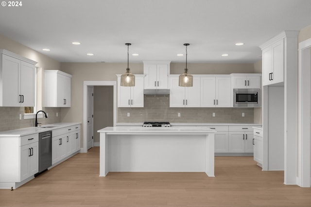 kitchen with under cabinet range hood, a sink, light wood-style flooring, backsplash, and stainless steel appliances