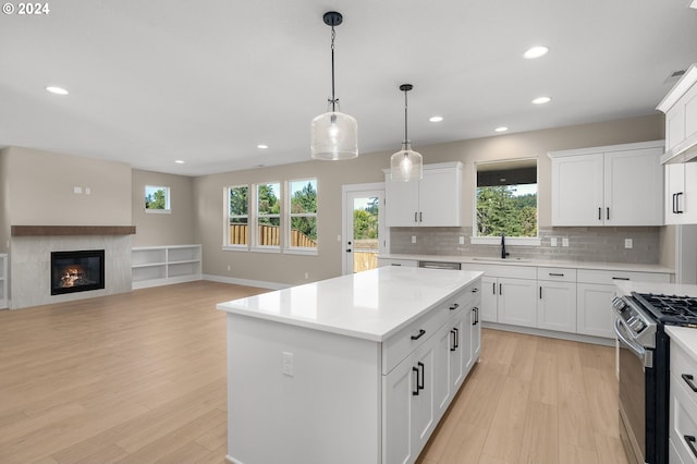 kitchen with stainless steel range with gas cooktop, a sink, light wood finished floors, and light countertops