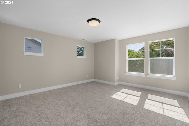 carpeted spare room featuring baseboards, visible vents, and a wealth of natural light