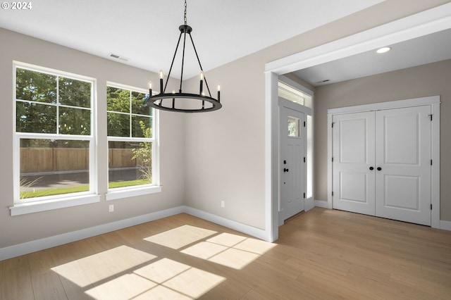 unfurnished dining area featuring baseboards, a chandelier, visible vents, and light wood-style floors