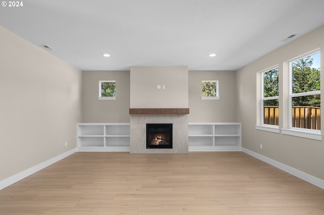 unfurnished living room featuring visible vents, recessed lighting, light wood finished floors, and a warm lit fireplace