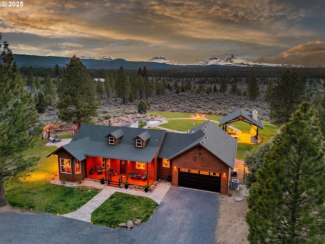16830 Delicious St, Bend, OR 97703 - view of front of property with a porch, a mountain view, an attached garage, a shingled roof, and a wooded view