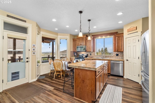 kitchen with brown cabinets, a sink, a center island, stainless steel appliances, and backsplash