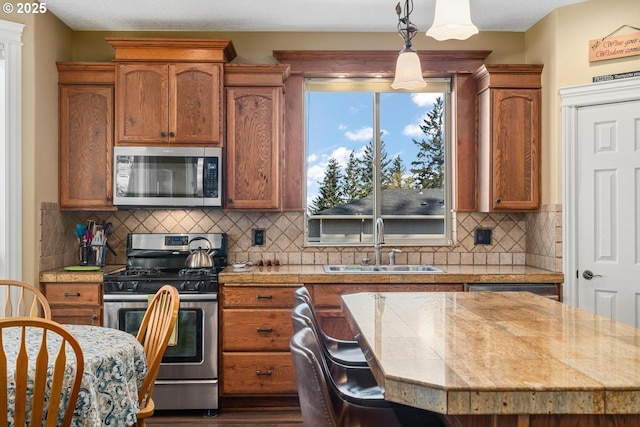 kitchen with brown cabinetry, backsplash, appliances with stainless steel finishes, a sink, and light countertops