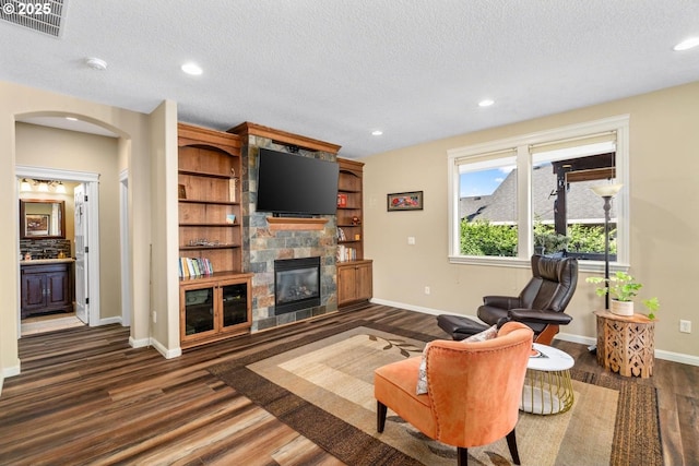 living room featuring wood finished floors, a stone fireplace, baseboards, recessed lighting, and arched walkways