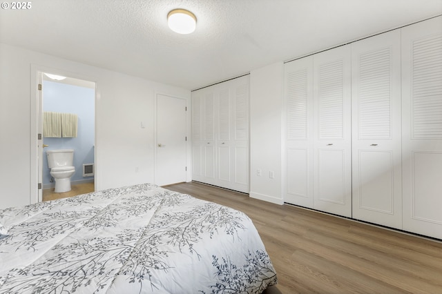 bedroom featuring hardwood / wood-style floors, two closets, a textured ceiling, and ensuite bath