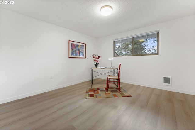 home office with a textured ceiling and light hardwood / wood-style flooring