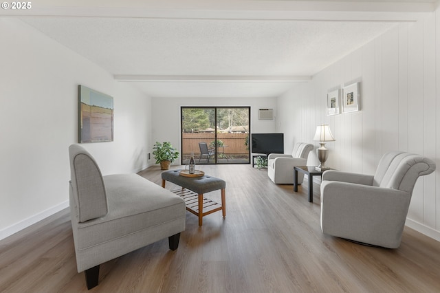 living room featuring wood-type flooring, a wall unit AC, a textured ceiling, and beam ceiling