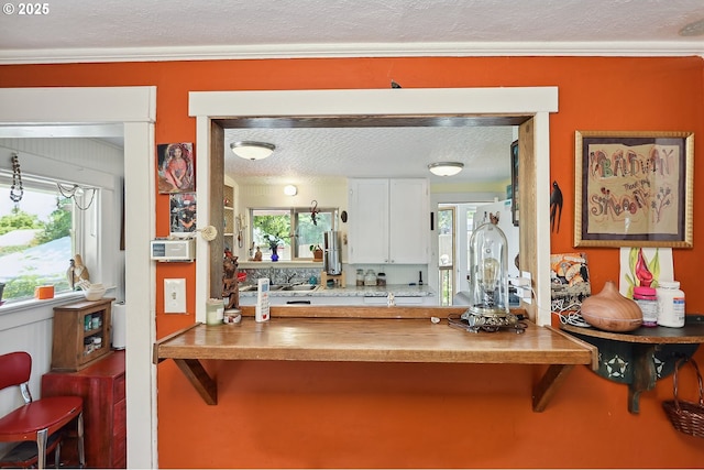 317 E 14th St, The Dalles, OR 97058 - kitchen featuring a textured ceiling, ornamental molding, white cabinets, plenty of natural light, and a breakfast bar area