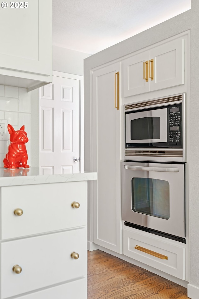 kitchen with white cabinetry, light stone countertops, stainless steel appliances, and light wood finished floors