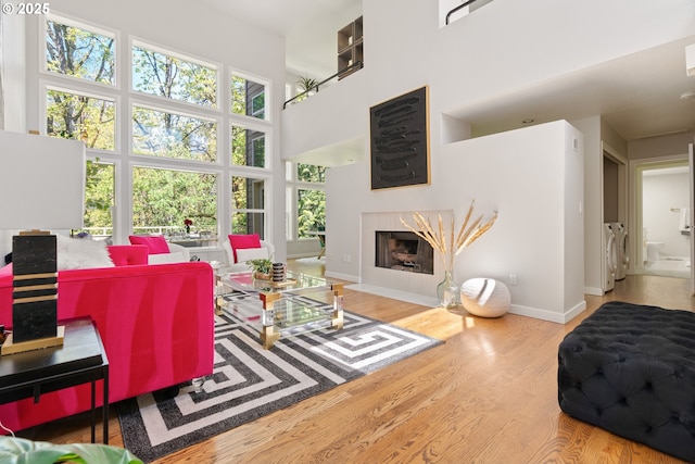 living room with washing machine and dryer, baseboards, wood finished floors, a high ceiling, and a fireplace