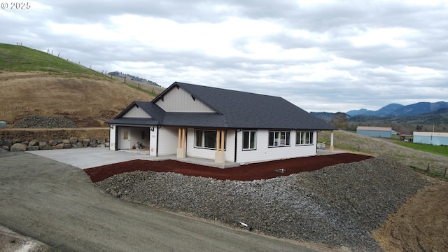 view of front of home with board and batten siding, concrete driveway, a mountain view, and roof with shingles