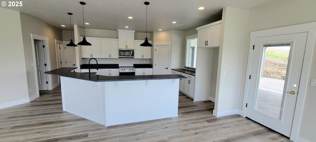 kitchen featuring stainless steel appliances, dark countertops, a large island with sink, and white cabinets