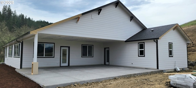 back of house featuring an attached carport, a patio, and roof with shingles