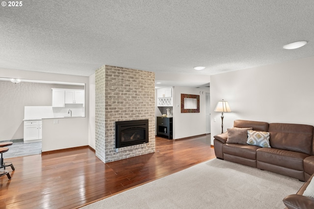 living room with a textured ceiling, sink, a brick fireplace, and light wood-type flooring