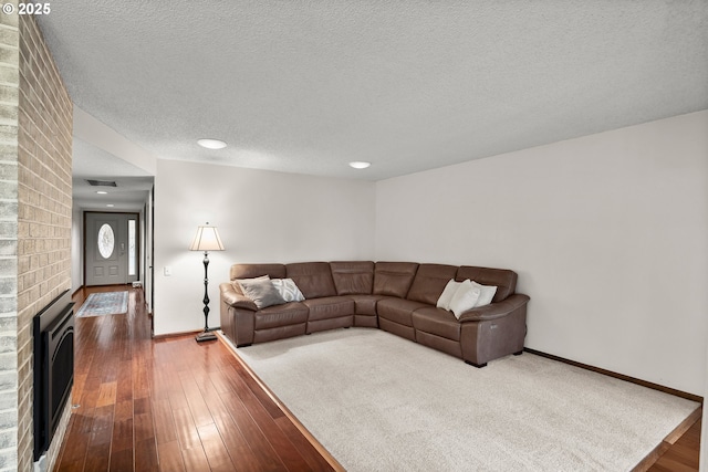 living room featuring wood-type flooring, a brick fireplace, and a textured ceiling