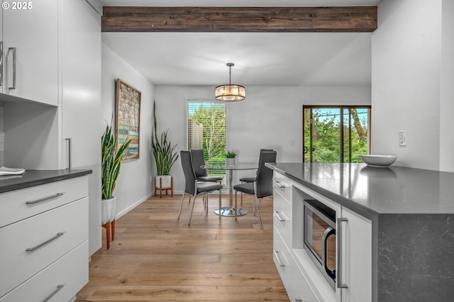 dining room with beam ceiling, light wood-style flooring, and baseboards