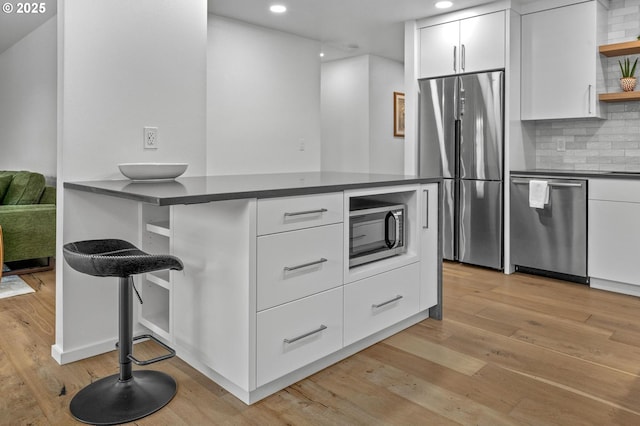 kitchen featuring light wood finished floors, white cabinets, dark countertops, stainless steel appliances, and open shelves