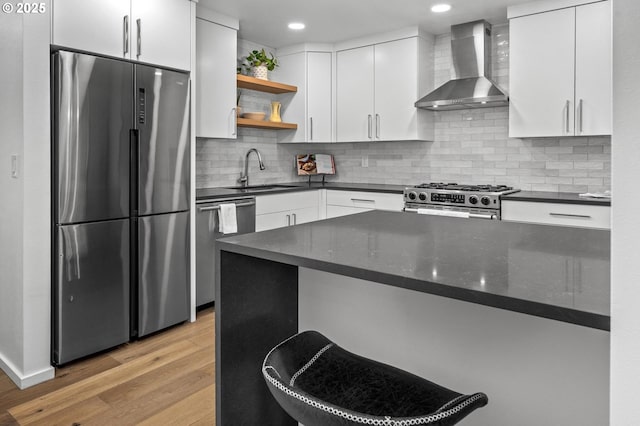 kitchen with wall chimney exhaust hood, light wood-style flooring, stainless steel appliances, open shelves, and a sink