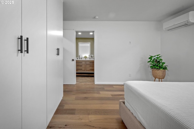 bedroom featuring connected bathroom, baseboards, an AC wall unit, and wood finished floors