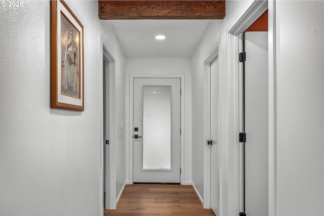 hall featuring light wood-style floors, baseboards, and a textured wall