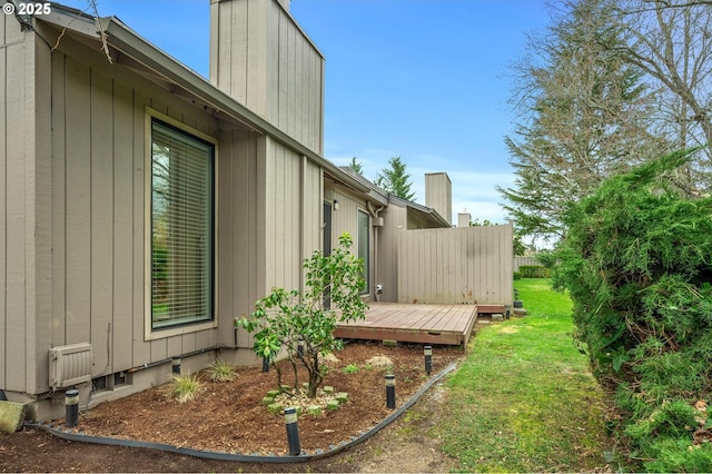 view of home's exterior with a lawn, a chimney, a wooden deck, and fence