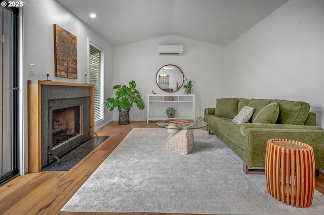 living room with a wall unit AC, a fireplace with flush hearth, vaulted ceiling, and wood finished floors