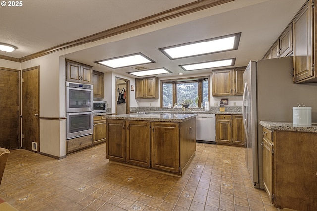 21445 NE Ornduff Rd, Hillsboro, OR 97123 - kitchen with appliances with stainless steel finishes, ornamental molding, stone counters, a kitchen island, and brown cabinetry