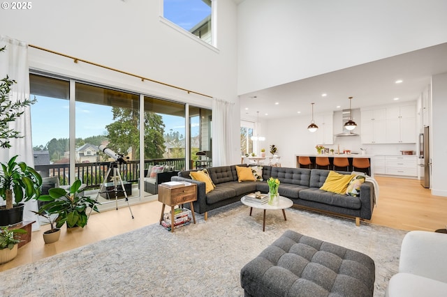 living room with light wood-type flooring, a towering ceiling, and recessed lighting