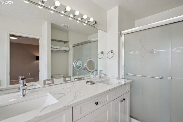 bathroom with a stall shower, double vanity, and a textured ceiling