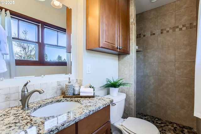 bathroom featuring tasteful backsplash, vanity, a tile shower, and toilet