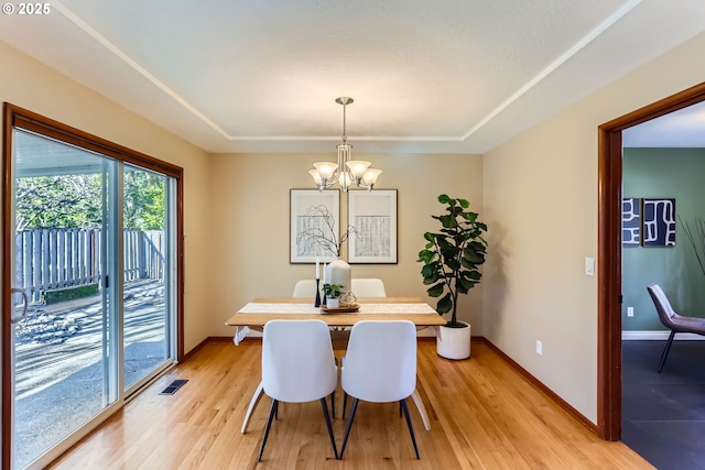 dining room with a raised ceiling, a chandelier, and light wood-type flooring