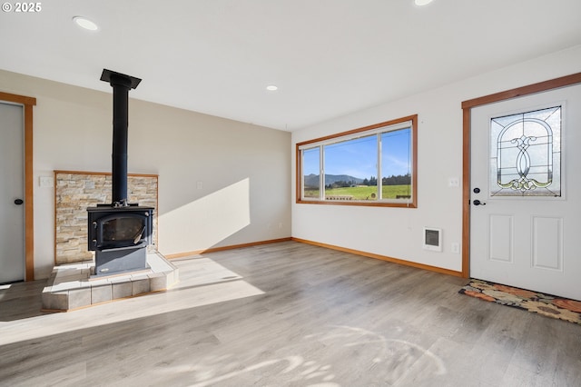 entrance foyer with heating unit, wood-type flooring, plenty of natural light, and a wood stove