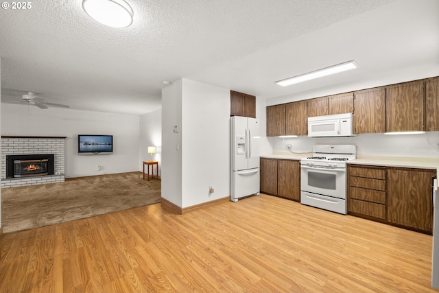 kitchen featuring a brick fireplace, open floor plan, light wood-type flooring, light countertops, and white appliances