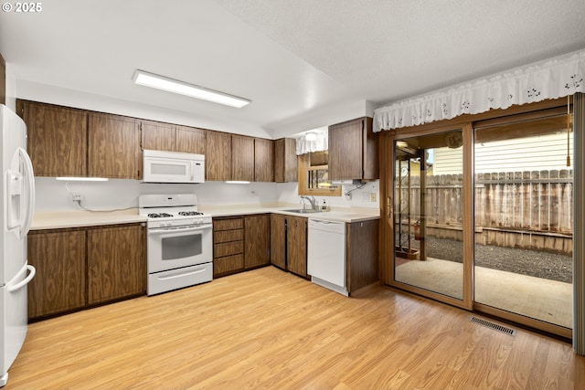 kitchen with visible vents, light countertops, light wood-type flooring, white appliances, and a sink