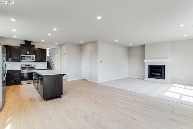 kitchen featuring light wood-style floors, stainless steel appliances, a center island, a glass covered fireplace, and recessed lighting