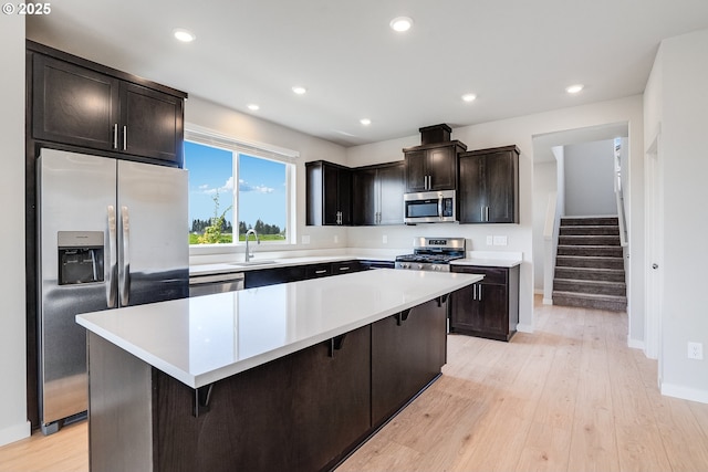 kitchen with light wood-style flooring, appliances with stainless steel finishes, light countertops, a kitchen bar, and a sink