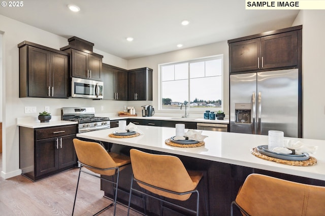 kitchen with a kitchen breakfast bar, a sink, stainless steel appliances, light countertops, and light wood finished floors