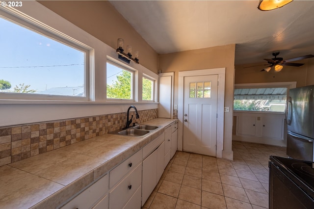 kitchen with white cabinets, a sink, freestanding refrigerator, tile countertops, and black / electric stove