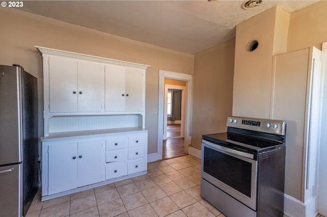 kitchen with light tile patterned floors, baseboards, appliances with stainless steel finishes, and white cabinetry