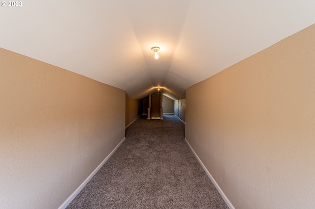 hallway with dark colored carpet and lofted ceiling