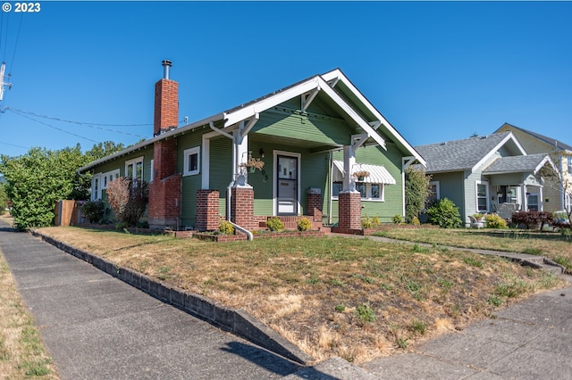 view of front facade featuring a chimney, a porch, and a front yard