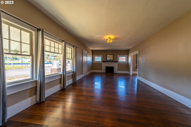 unfurnished living room with a fireplace, baseboards, and dark wood-type flooring