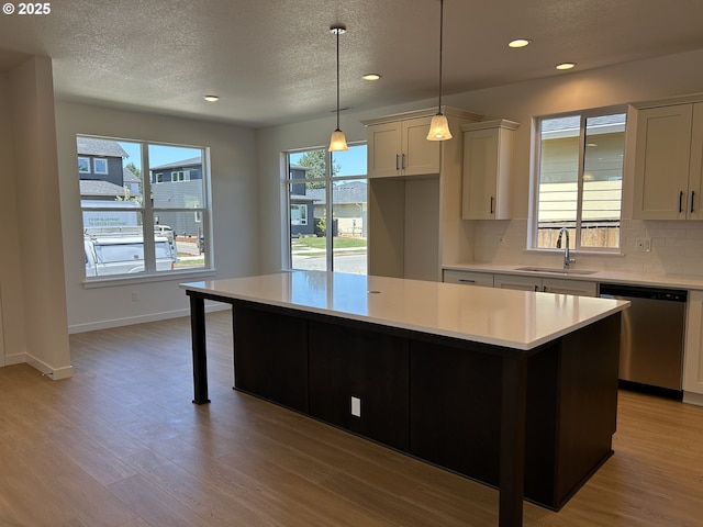 2940 Olympic St Unit 21, Woodburn, OR 97071 - kitchen with stainless steel dishwasher, light countertops, a sink, light wood-style flooring, and a textured ceiling