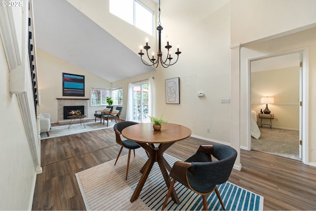 dining space featuring a lit fireplace, high vaulted ceiling, a chandelier, dark wood-type flooring, and baseboards