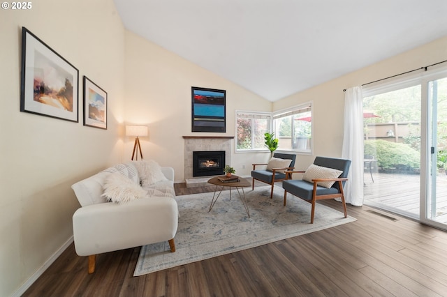 living area featuring a tiled fireplace, lofted ceiling, plenty of natural light, wood finished floors, and baseboards